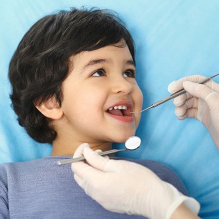 young boy smiling while dentist looks at teeth   
