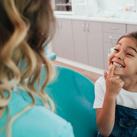 young girl smiling and pointing to teeth    