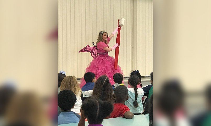 Dental team member dressed as a tooth fairy holding oversized toothbrush