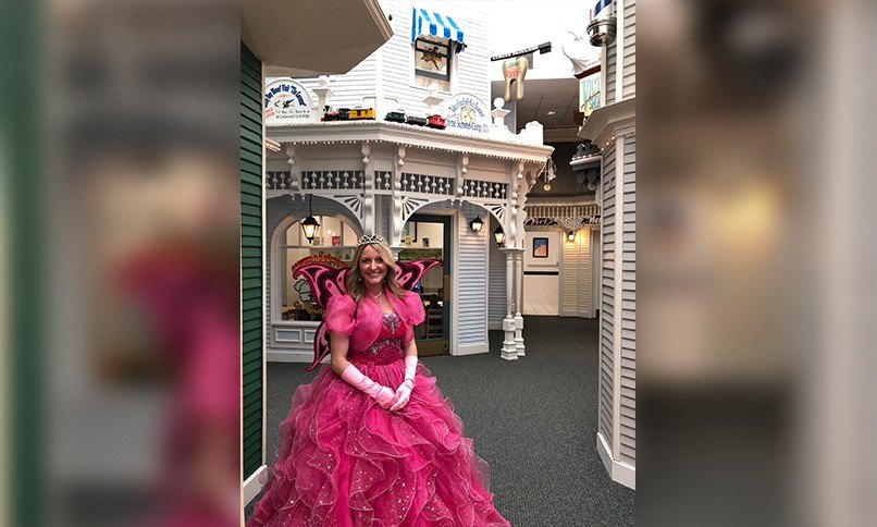 Dental team member dressed as tooth fairy in front of old fashioned dental office building