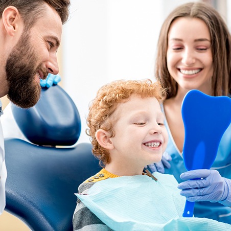 A young boy looking at his toothy smile alongside a dentist