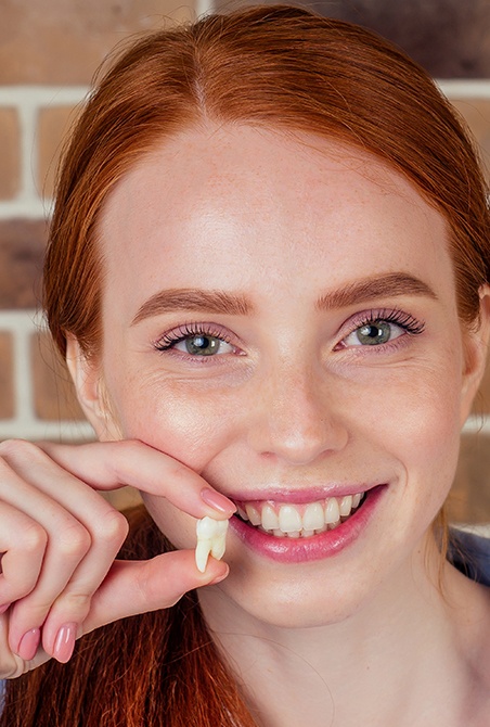 Young woman holding up tooth after extraction