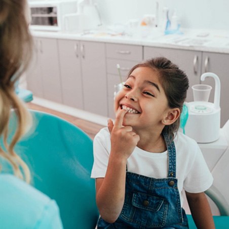 young girl smiling and pointing to teeth 