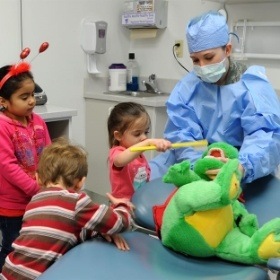 Pediatric dental team member using toy to show kids in Wylie how to brush teeth
