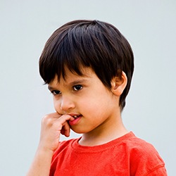 Young boy in red shirt biting his fingernails
