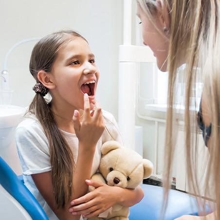 Little girl receiving dental sealants pointing at her teeth