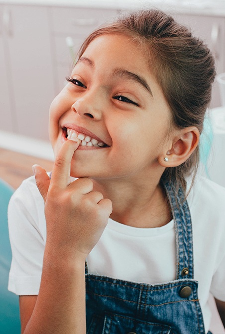 Little girl pointing to smile after restorative dentistry