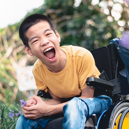 smiling boy in a wheelchair picking flowers outside