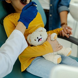 a child holding a teddy bear in a dental chair