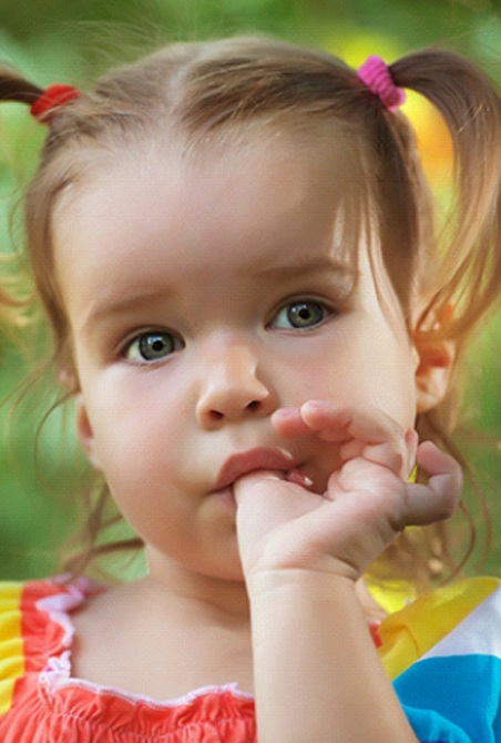 A little girl wearing a colorful blouse and pigtails engages in thumb-sucking in Wylie