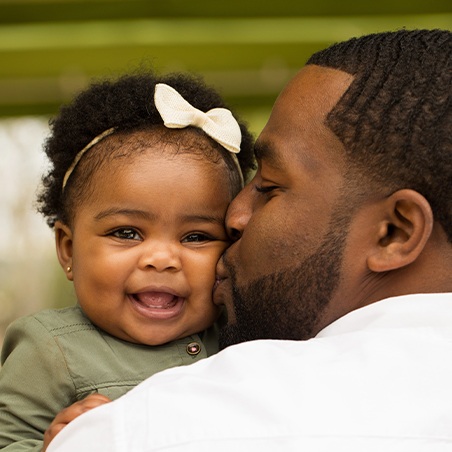 Father giving baby girl a kiss on the cheek after dentistry for infants