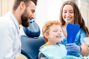 little boy looking in a tooth-shaped mirror at his pediatric dentist’s office 