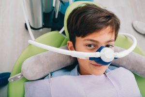 a child smiling while sitting in a dental chair with a nitrous oxide nose mask on their face