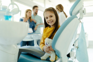 Child sitting the patient’s chair and holding a teddy bear