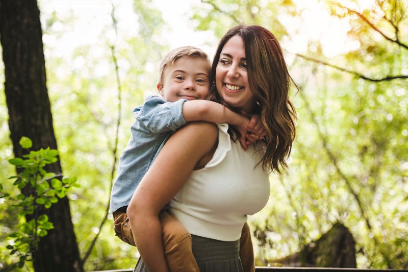 woman carrying a little boy with Down syndrome on her back and smiling