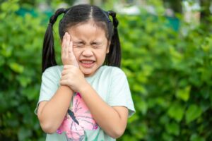 Child wincing in severe pain and holding right side of face.